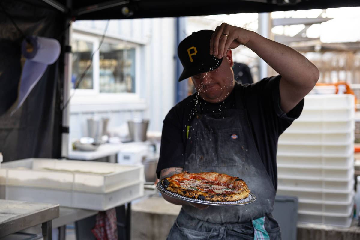 a pizza maker scattering seasoning over the top of a freshly baked pizza