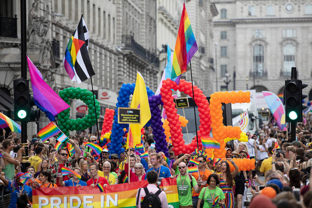 festejantes no desfile do Orgulho em Londres, a percorrer a cidade com bandeiras coloridas e um enorme balão com a palavra «pride» composto pelas cores da bandeira do Orgulho
