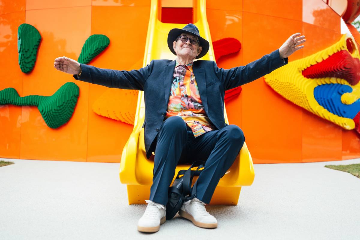Sir Peter Cook sat on the end of a slide attached to the new play pavilion in Kensington Gardens