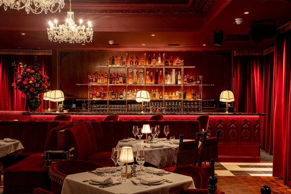 een bougie, laag verlicht restaurant met roodgekleurd decor en kleine lampjes op elke tafel die een zachte gloed werpen