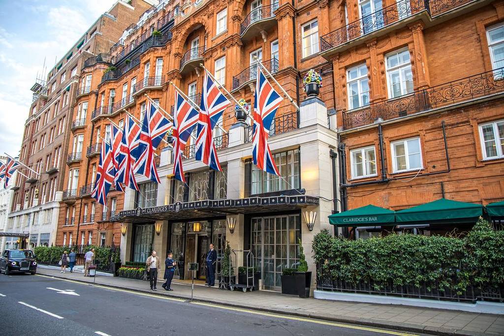 The exterior of Claridge's Hotel with a doorman outside adn Union Jack flags flying above the entrance