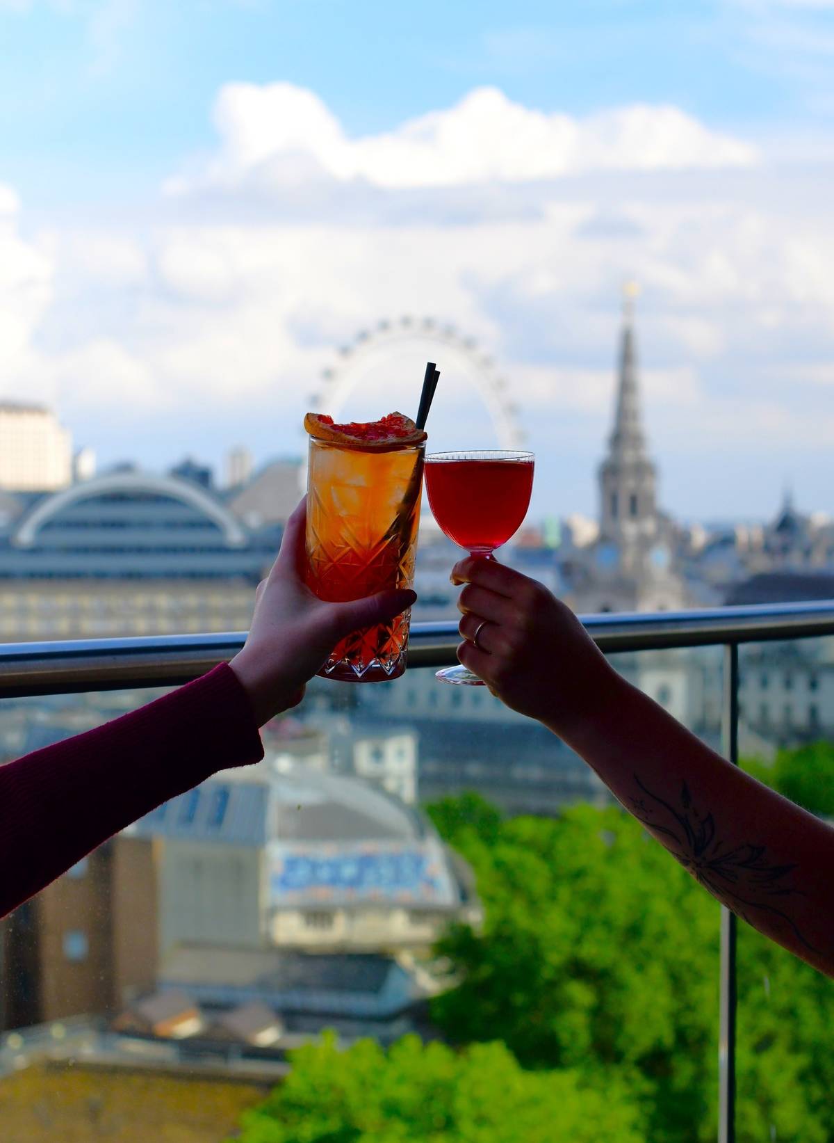 two cocktails being cheersed in front of a view of london, including the london eye
