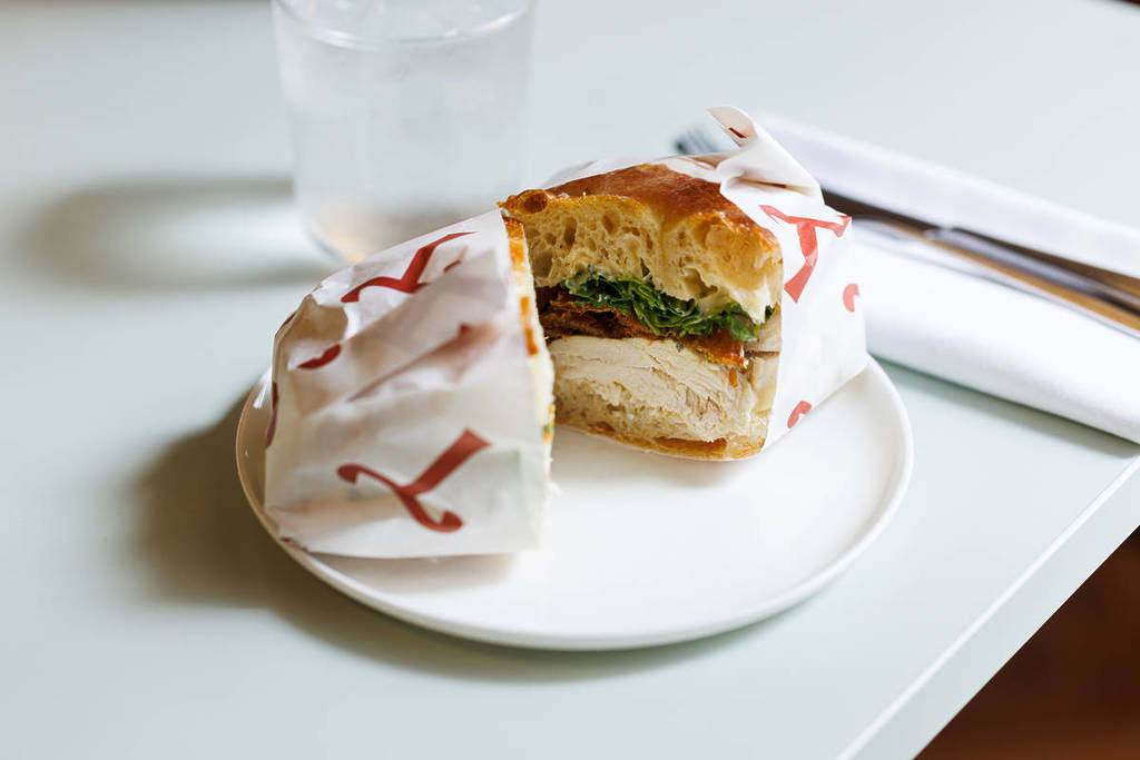 un bocadillo envuelto en papel sulfurizado, cortado por la mitad y presentado en un plato para mostrar los rellenos