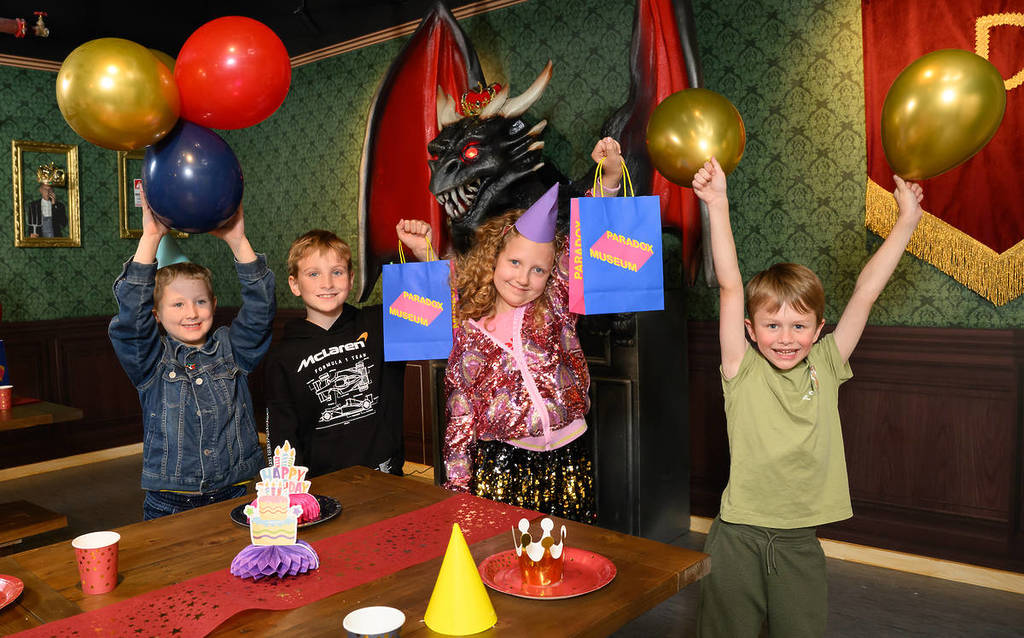a group of kids hold up party bags and balloons at the Paradox Museum party room