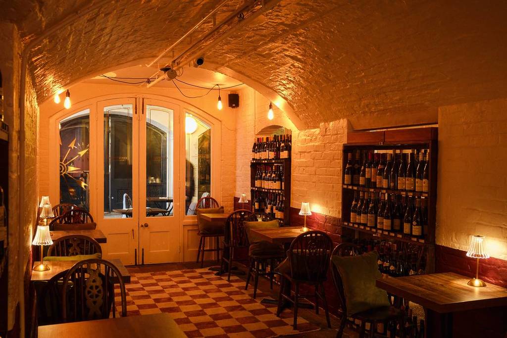 Un bar en penumbra con botelleros, mesas y sillas