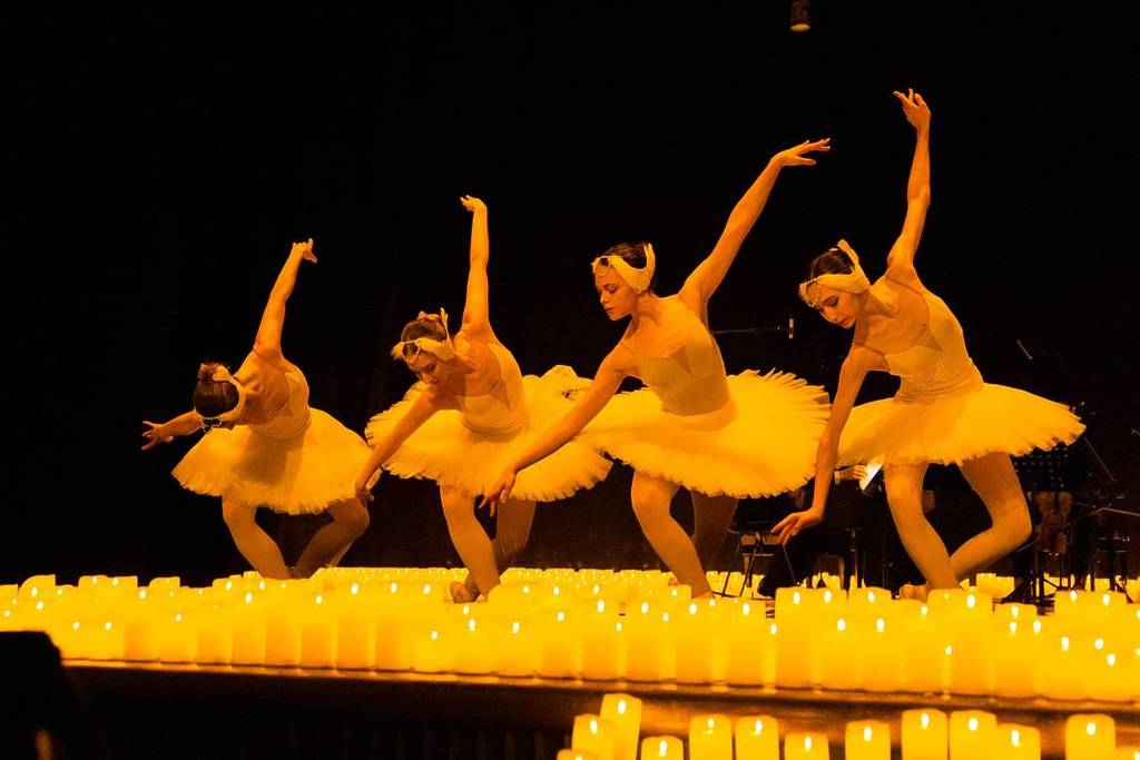 Four ballerinas performing on a raised stage bathed in candlelight