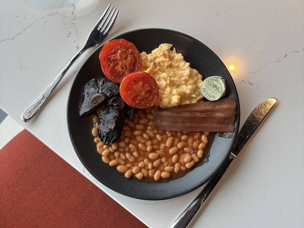 A buffet breakfast featuring beans, grilled mushrooms, grilled tomato, scrambled eggs, and vegetarian bacon.