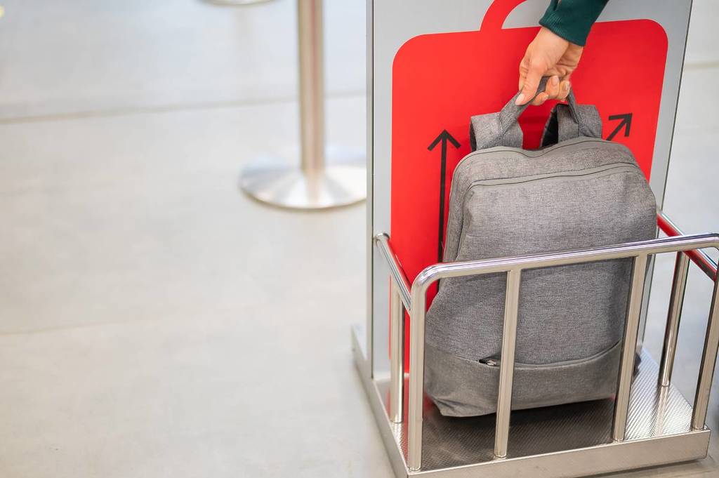 jemand, der sein Handgepäck in den Käfig stellt, um es am Flughafen auf seine Größe zu überprüfen
