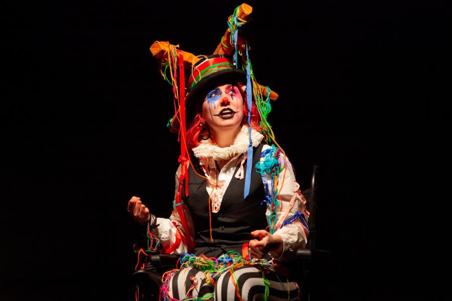 a performer in a wheelchair dressed in a clown outfit photographed mid-performance