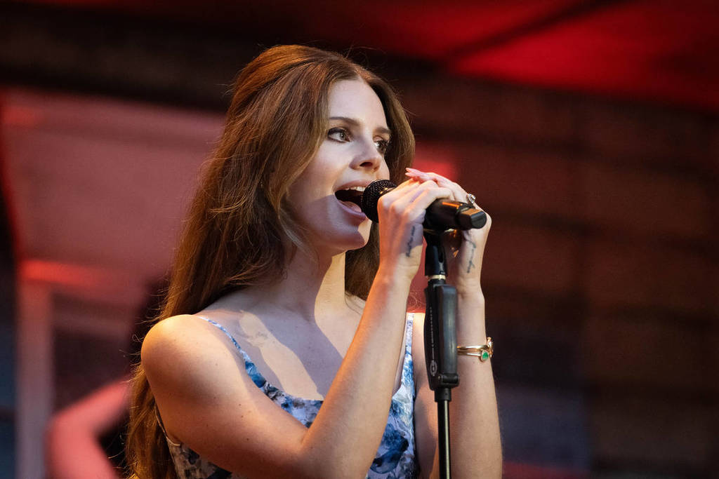 lana del rey actuando en el escenario agarrada al micrófono del atril