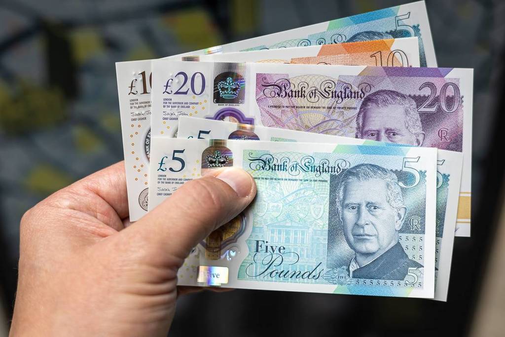 Primo piano di una mano che tiene in mano le nuove banconote da 5, 10 e 20 sterline britanniche, con il re Carlo III