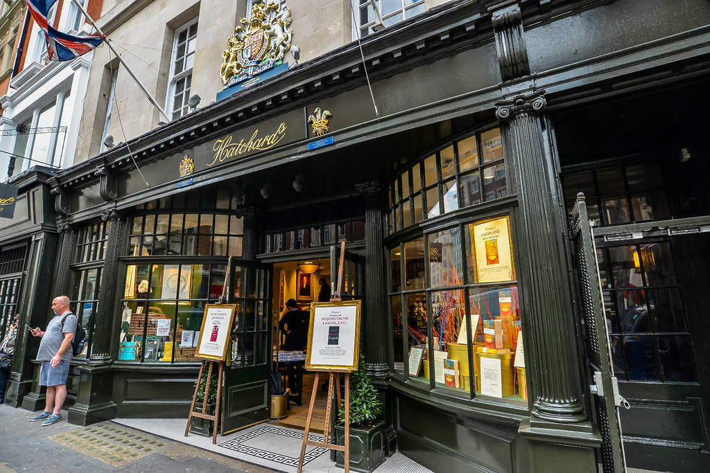 Bookshop front, from an angel. Painted black, regal. Royal coat of arms above the door on the first floor, a logo written in cursive gold underneath. Curved bay window evoke classiness.