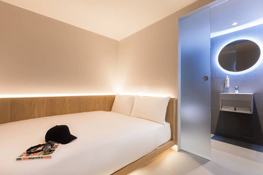 A clean, modern tiny hotel room. White walls, bright recessed lights, and a ultra modern bathroom.