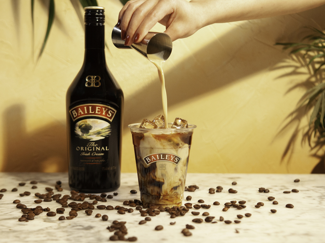 baileys being poured into an iced coffee drink, next to a bottle of baileys