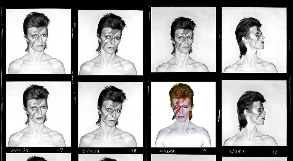 A black-and-white contact sheet featuring 16 portraits of David Bowie in his iconic 'Aladdin Sane' look, with slicked-back hair and a lightning bolt painted across his face. Most images are monochrome except for the center image, which is fully colored, showing Bowie with bright red hair, pale skin, and the red-and-blue lightning bolt makeup. He appears shirtless, with varied expressions and poses in each frame, facing different angles against a plain backdrop.