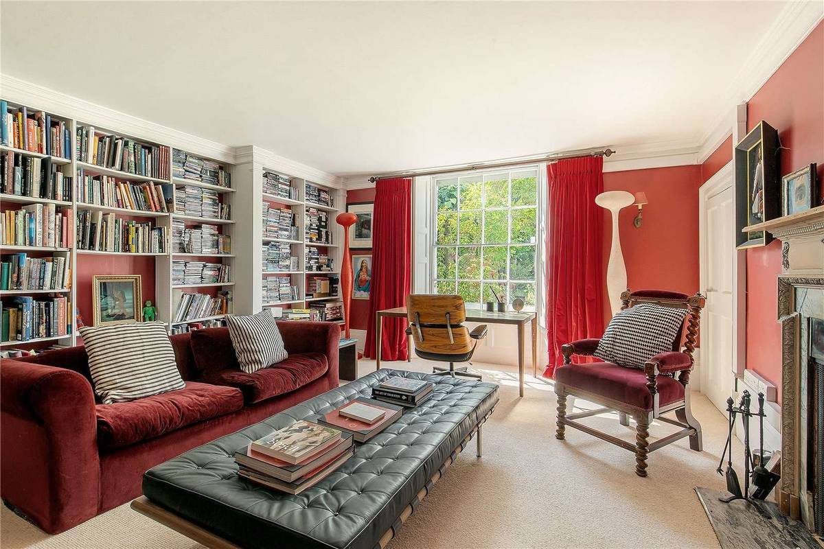 inside tim burton's english country home where you can see a library wall with shelves and books, a couch and coffee table and bay windows