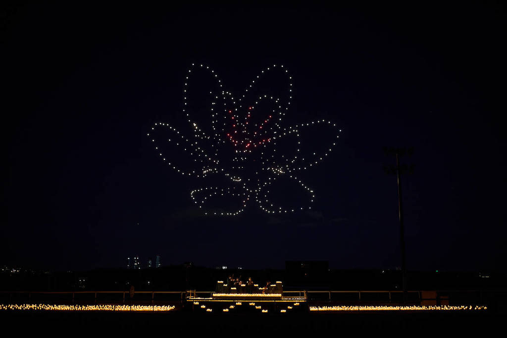 a vibrant flower created by hundreds of drone eppars in the sky over a string quartet performing by candlelight at the DroneArt Show