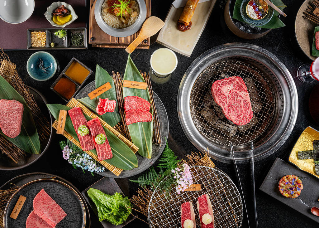 une table surchargée de morceaux de Wagyu et un steak en train de cuire sur un grill dans la table elle-même