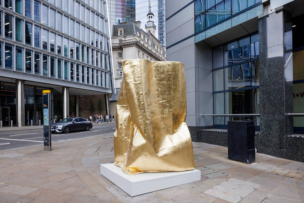 una escultura dorada de una simple bolsa de papel ampliada hasta alcanzar proporciones humanas.