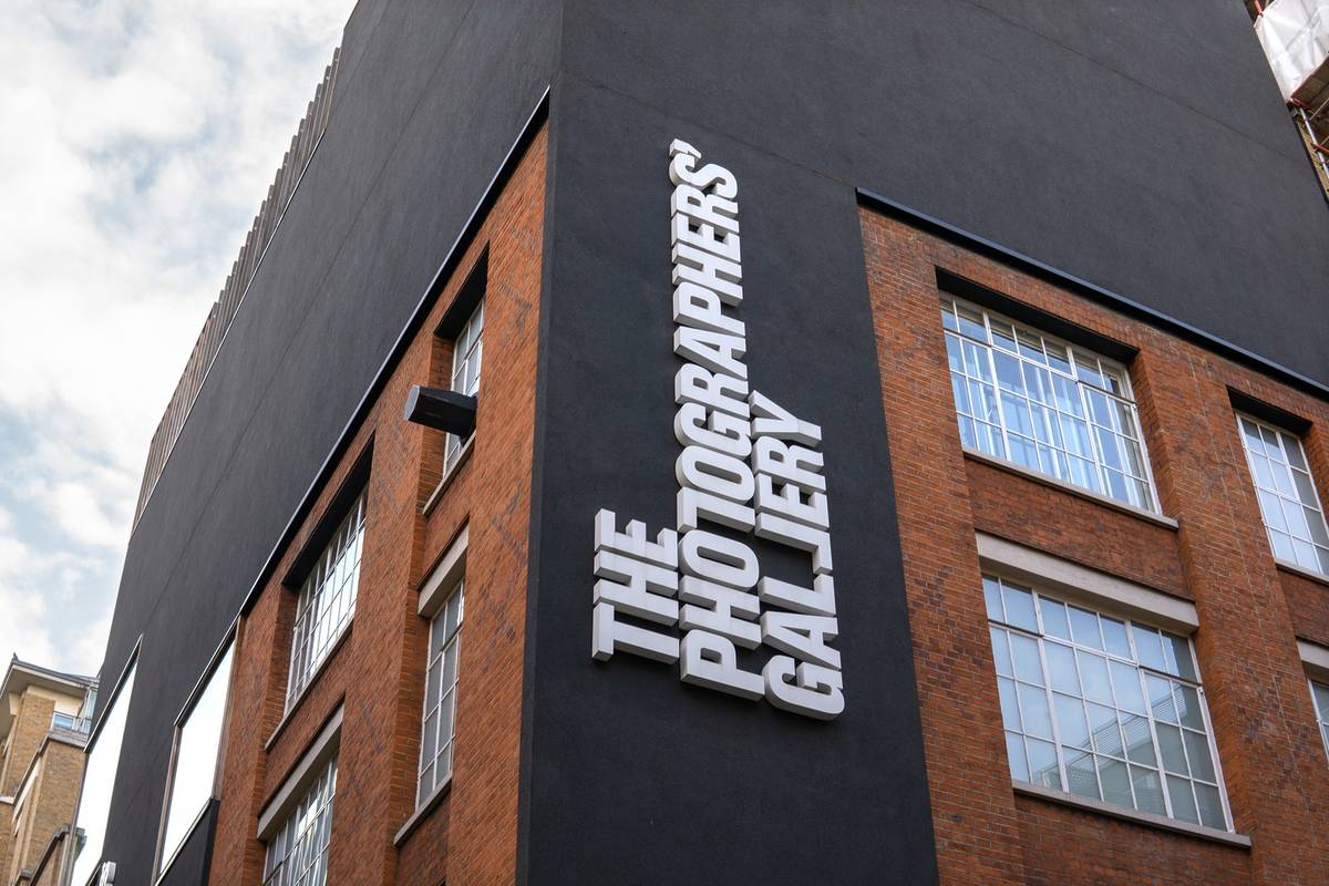The exterior of a building, at an angle, with a sideways text logo affixed to the building: THE PHOTOGRAPHERS' GALLERY. Warehouse-style windows are visible.