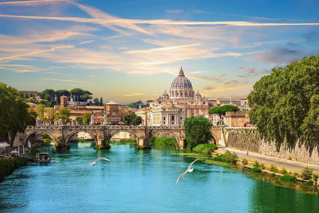 A view of a cathedral in Rome from across a bright blue river