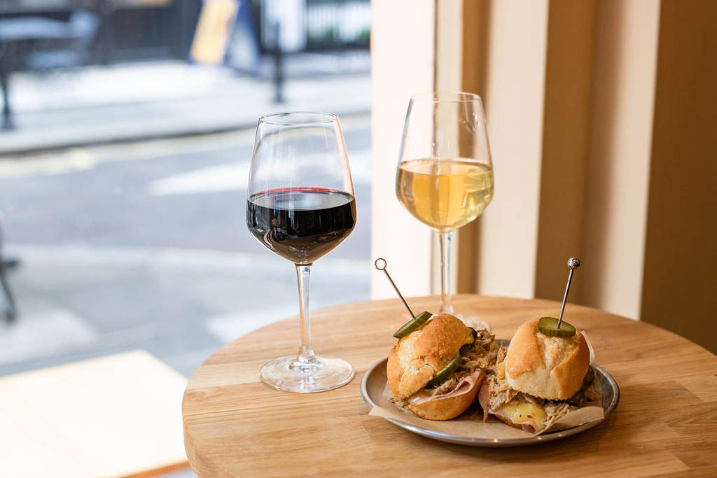 due mini panini su un piatto accanto a due bicchieri di vino, uno rosso e uno bianco