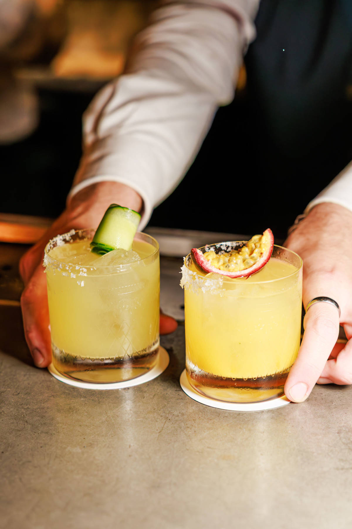 two spicy margaritas being placed on a table by a bartender, each crowned with a piece of fruit