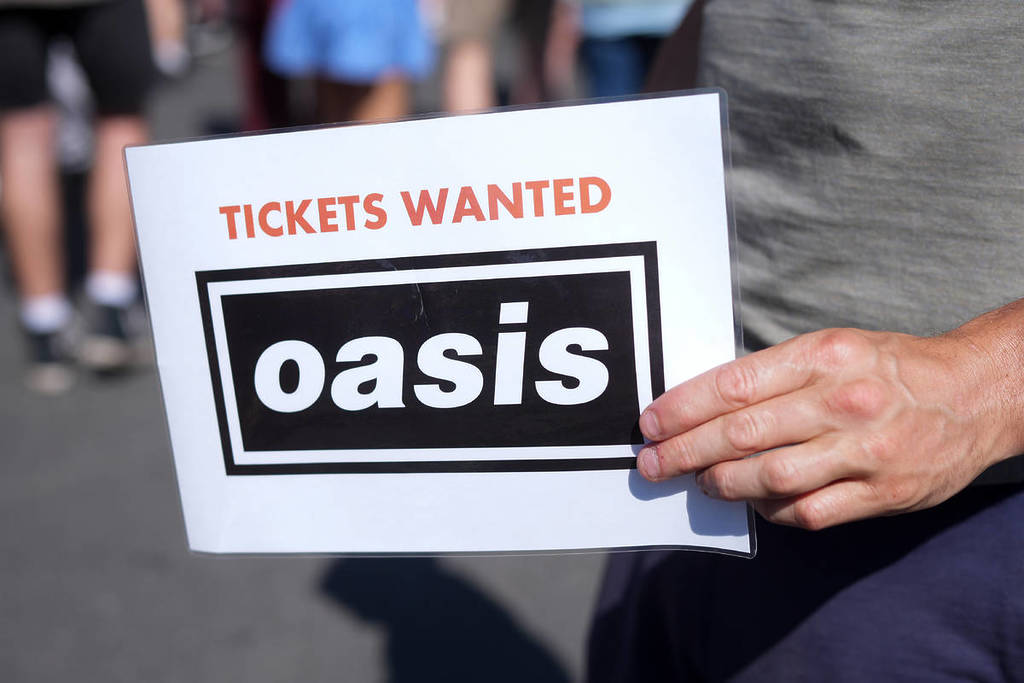 Oasis fan looking for tickets in Manchester with a sign saying 'Tickets Wanted'