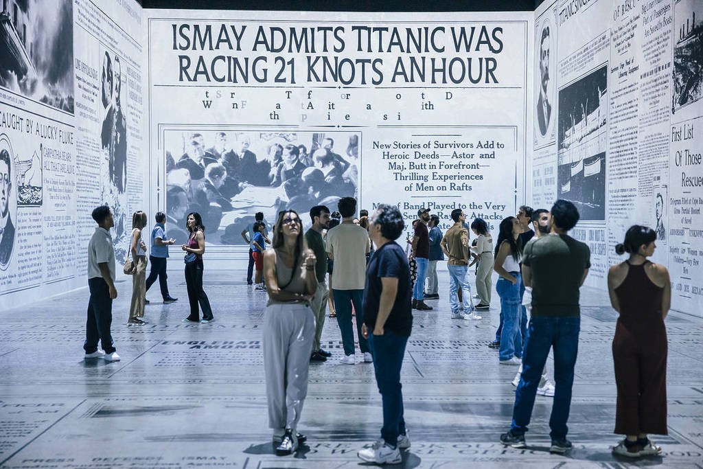 people look around a room with projection of newspaper clippings about the Titanic at the Legend of the Titanic exhibition