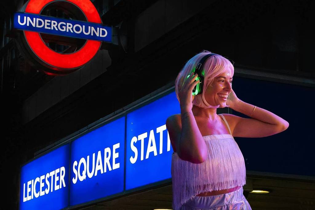 eine Dame mit Kopfhörern über einem Bild der Leicester Square Underground Station
