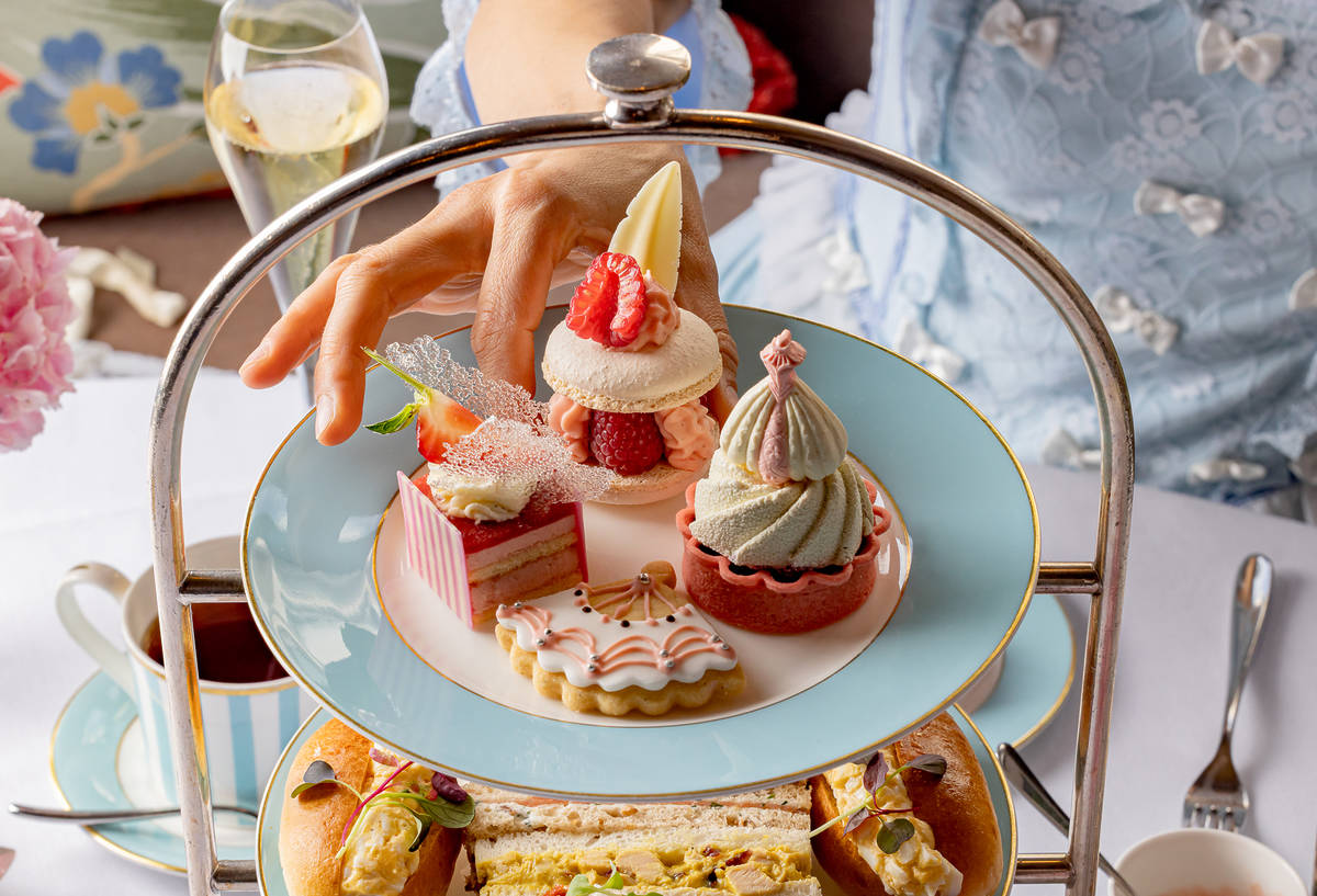 a hand reaching out to take a cake from a selection of sweet treats at a marie antoinette afternoon tea