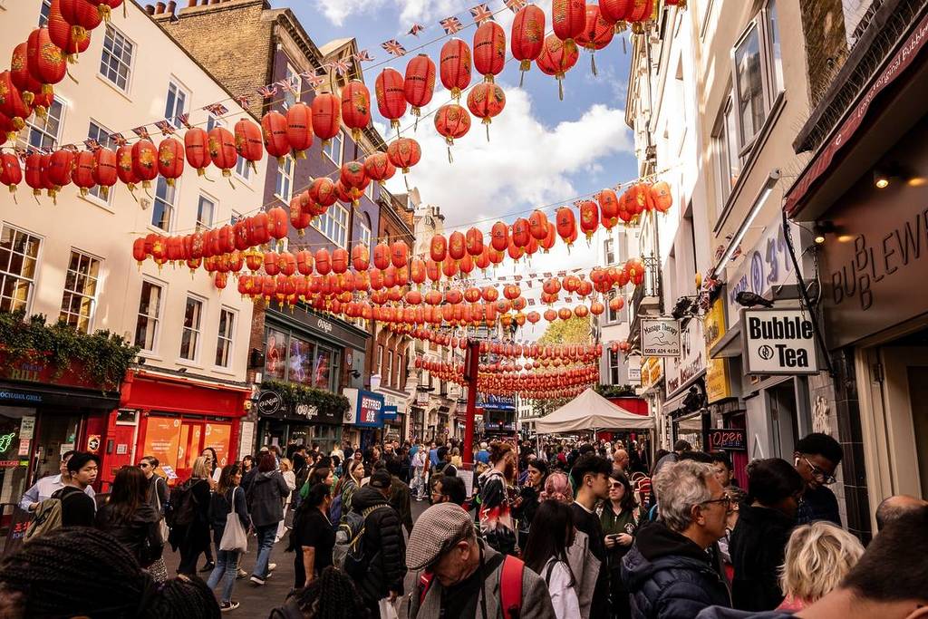 people milling about in the street in chinatown under the iconic red and yellow paper lanterns criss crossing the sky