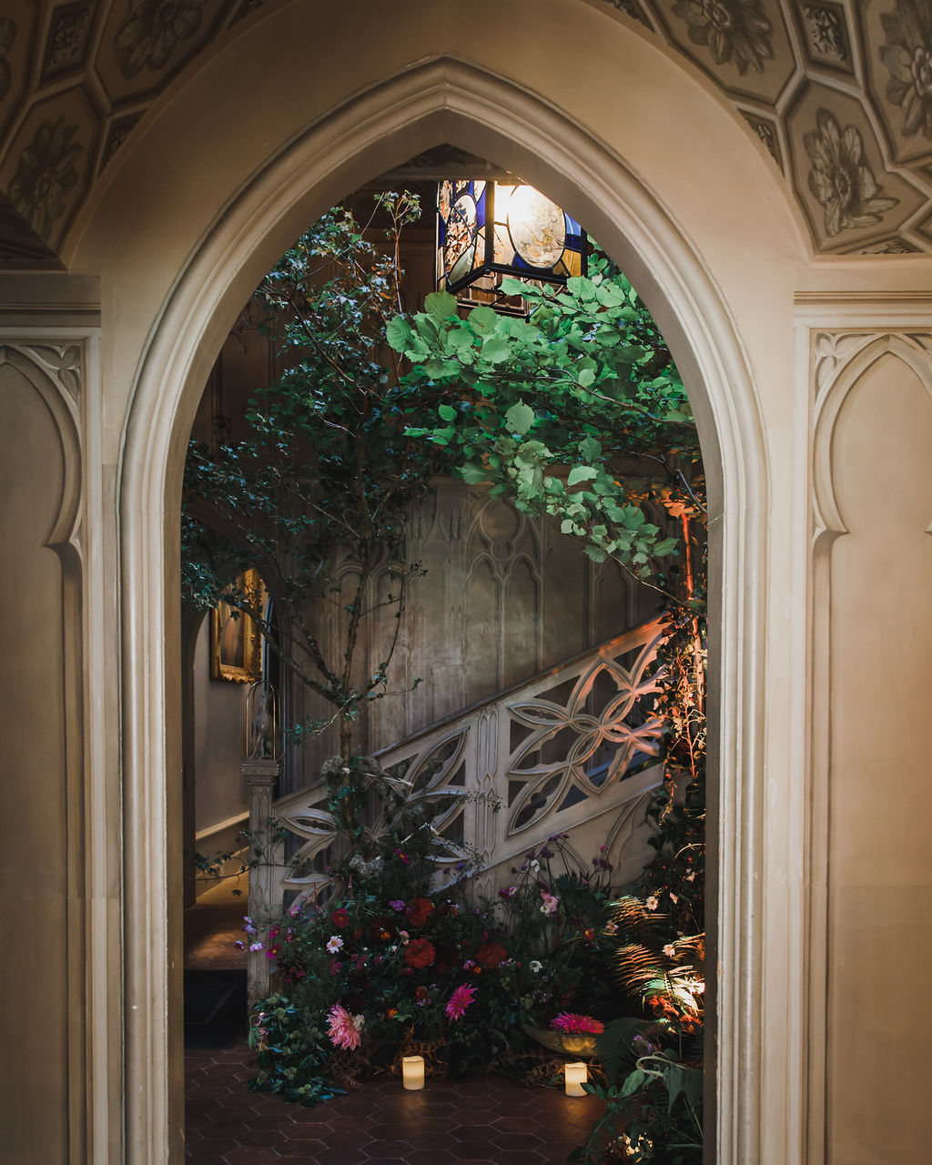 an archway leading to a room with a staircase and a tree, and an illuminated flower display