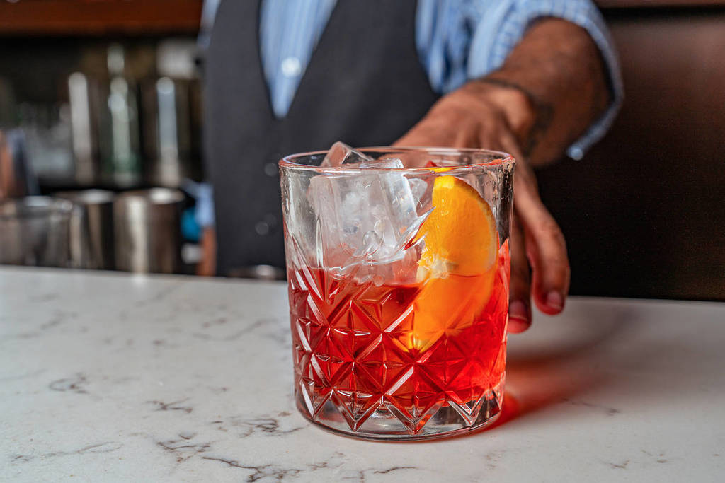 a negroni on a bar, being pushed forward by a bartender