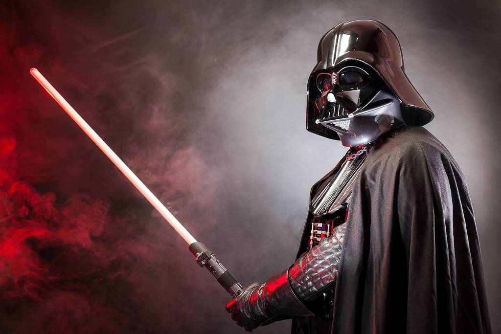 ortrait of Darth Vader costume replica with his sword . Darth Vader is a fictional character of Star Wars saga. Red grazing light and smoke