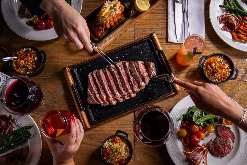 Wagyu steak being shared at Fazenda, with side dishes and cocktails on the table.