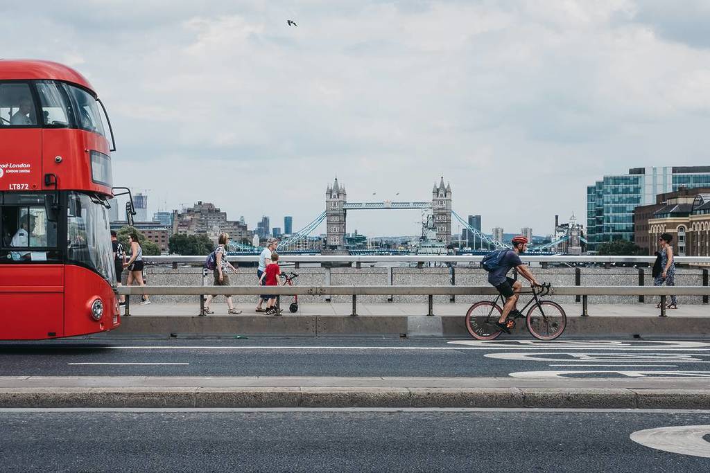 a bus and a cyclist crossing a bridge - with a view of Tower Bridge in the background