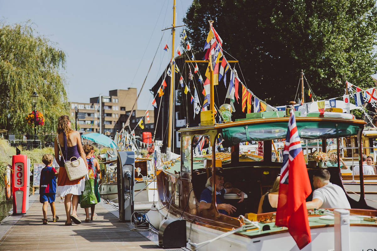 people walking past multiple moored boats with ornate bunting