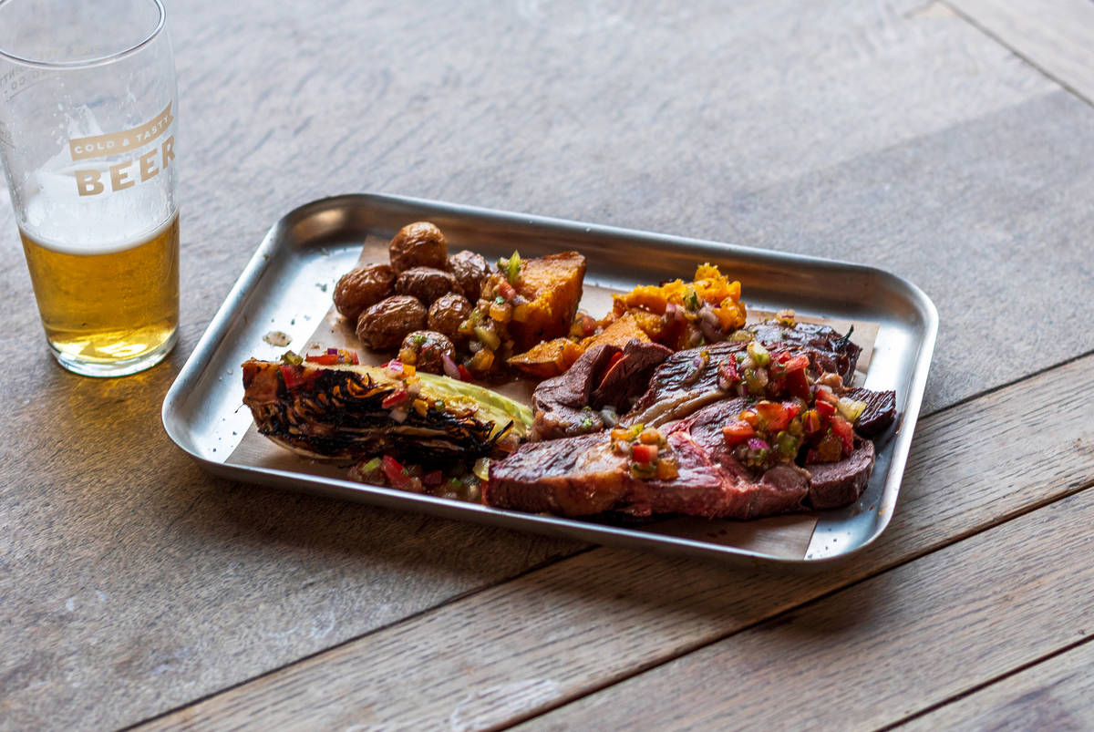 a platter of bbq'd food presented on a wooden table alongside a half-drunk pint of beer
