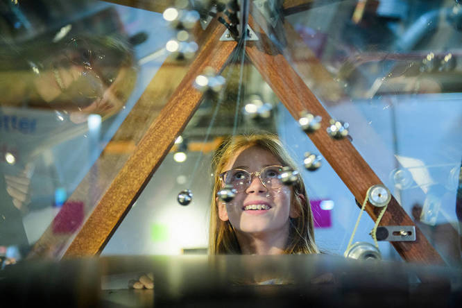 someone looking up at an array of suspended marbles and orbs in a triangular display case