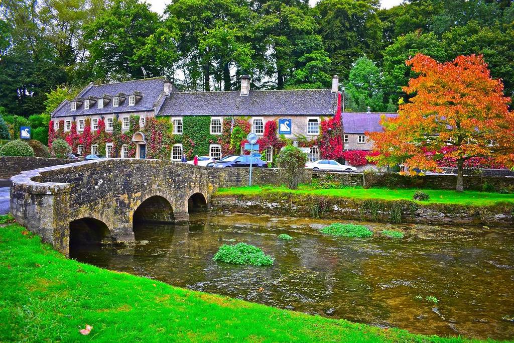 Bibury, Gloucestershire / Inglaterra - 21/09/2017: O Swan Hotel na bonita aldeia de Bibury, nos Cotswolds. Antiga ponte de pedra sobre o rio Coln.