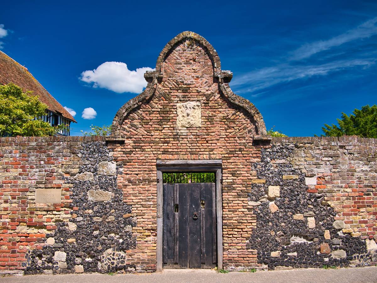Sandwich, UK - Jun 28 2022: An old wooden gate surrounded by an arch of rustic brickwork and stone facing on both sides. A plaque on the left is inscribed The King’s Lodging - Strand Street, Sandwich.