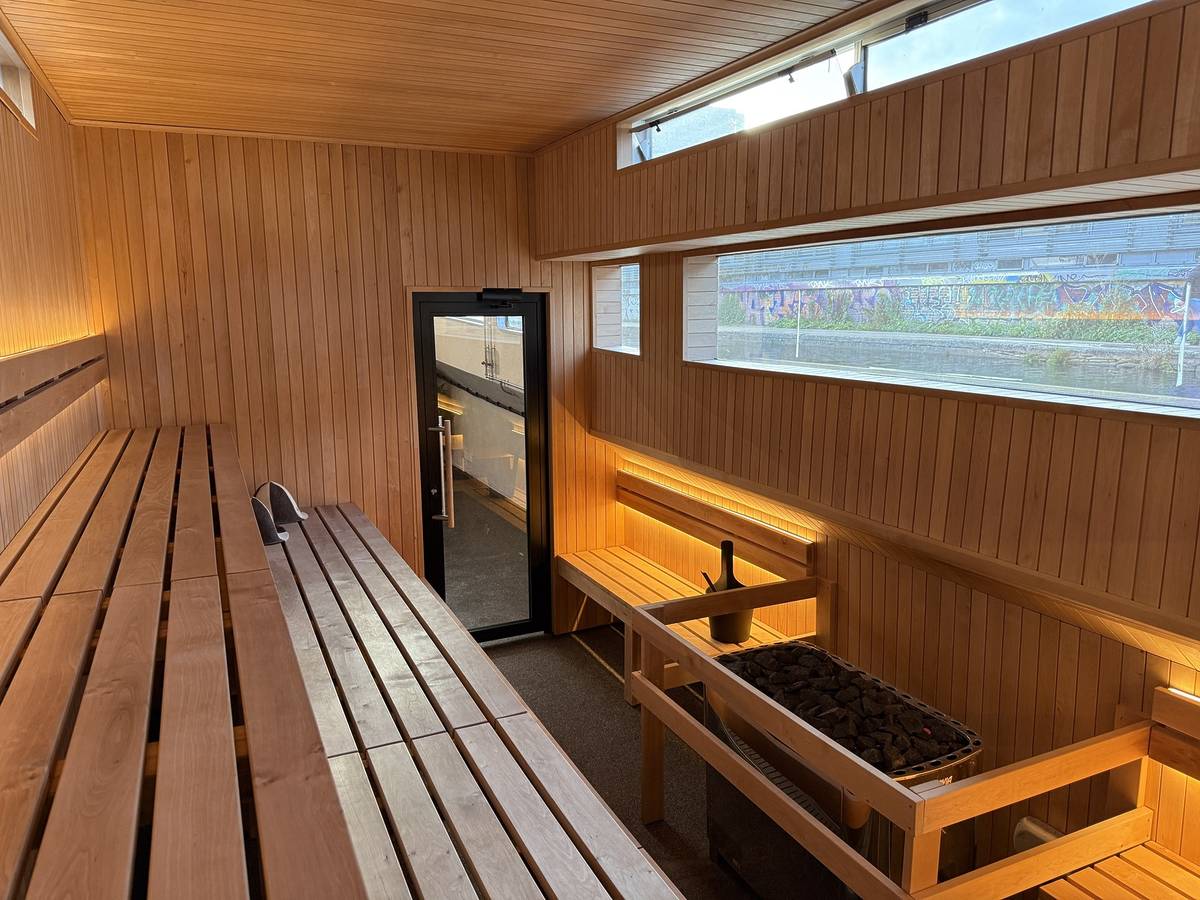 the wood panelled inside of a sauna on a boat, with a view of the water outside the boat through a wall-spanning window