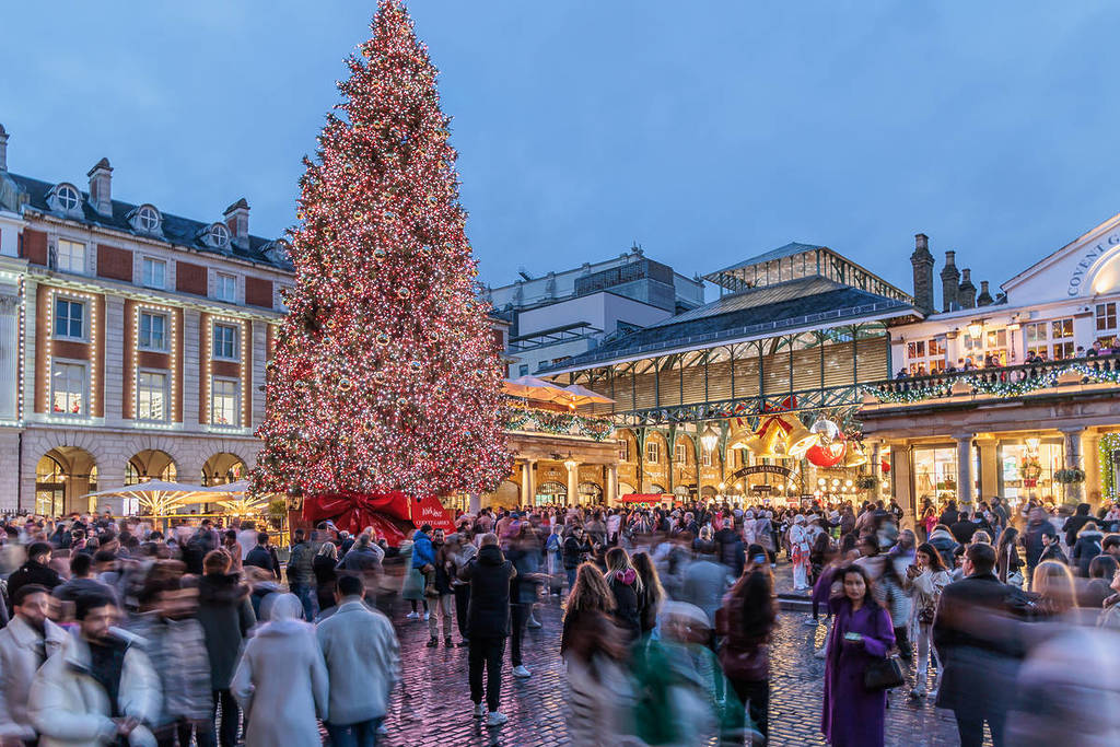 un albero di Natale che svetta su Covent Garden al tramonto, con centinaia di persone che si aggirano godendosi le decorazioni natalizie