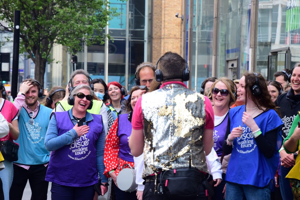 A host in a sparkly waistcoat leading a group of peple on a silent disco walking tour