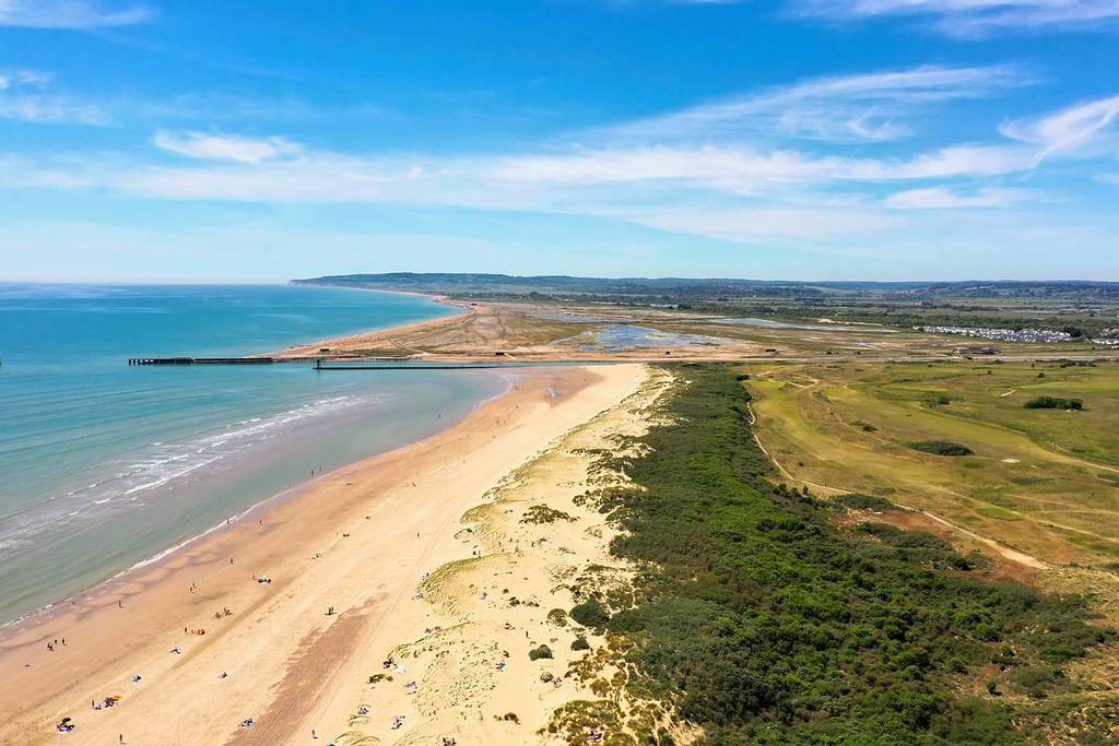 Ein langer Sandstrand mit dem Meer auf der einen Seite und viel Grün auf der anderen