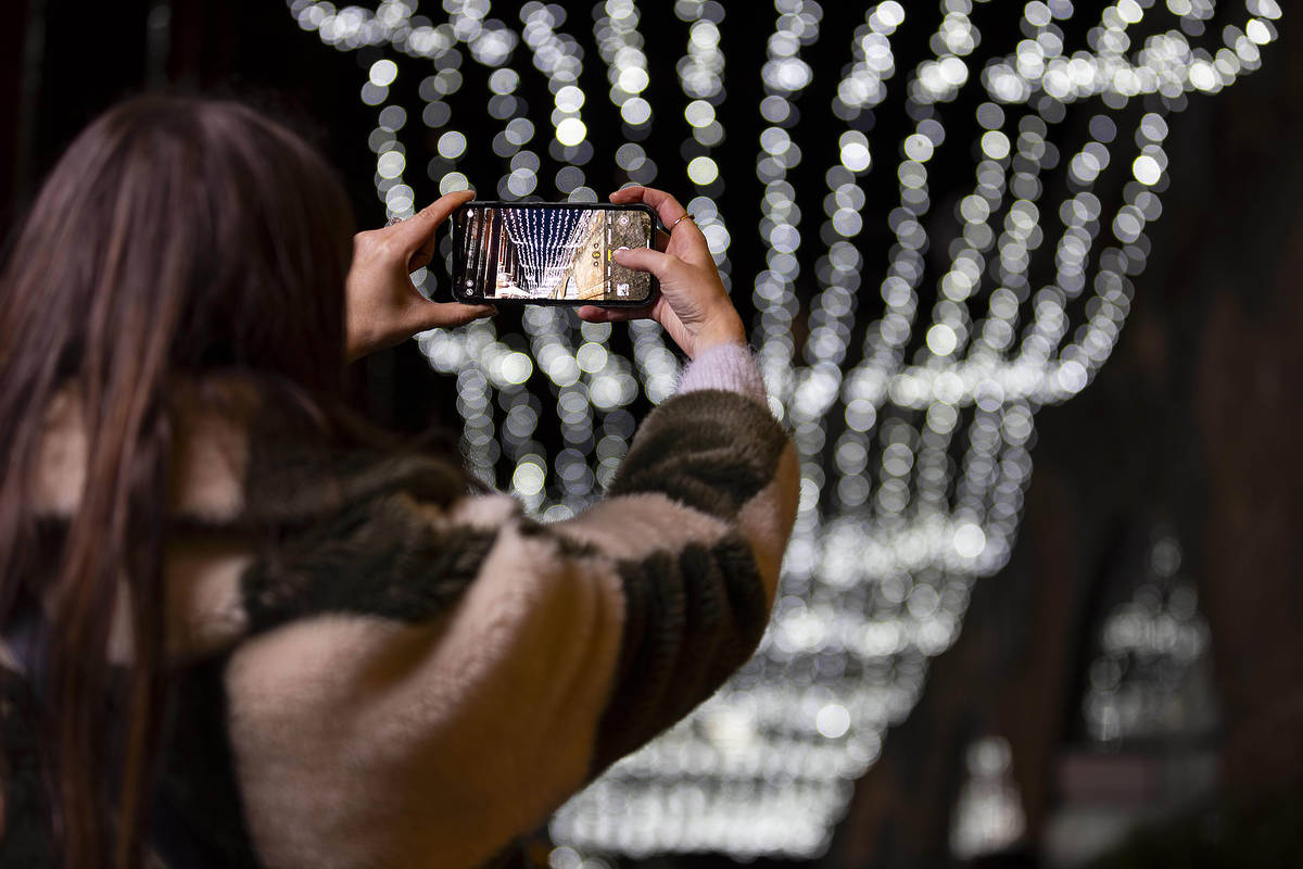 someone taking a photo of an overhead canopy of Christmas lights