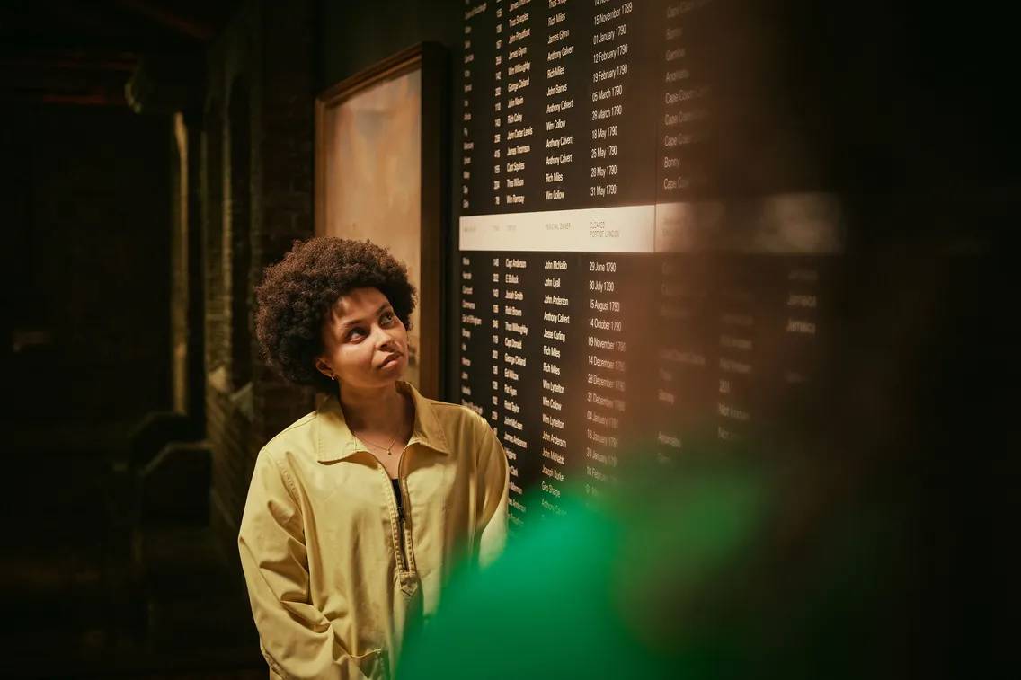 someone looking up at a list of names of people involved in the slave trade that went through london