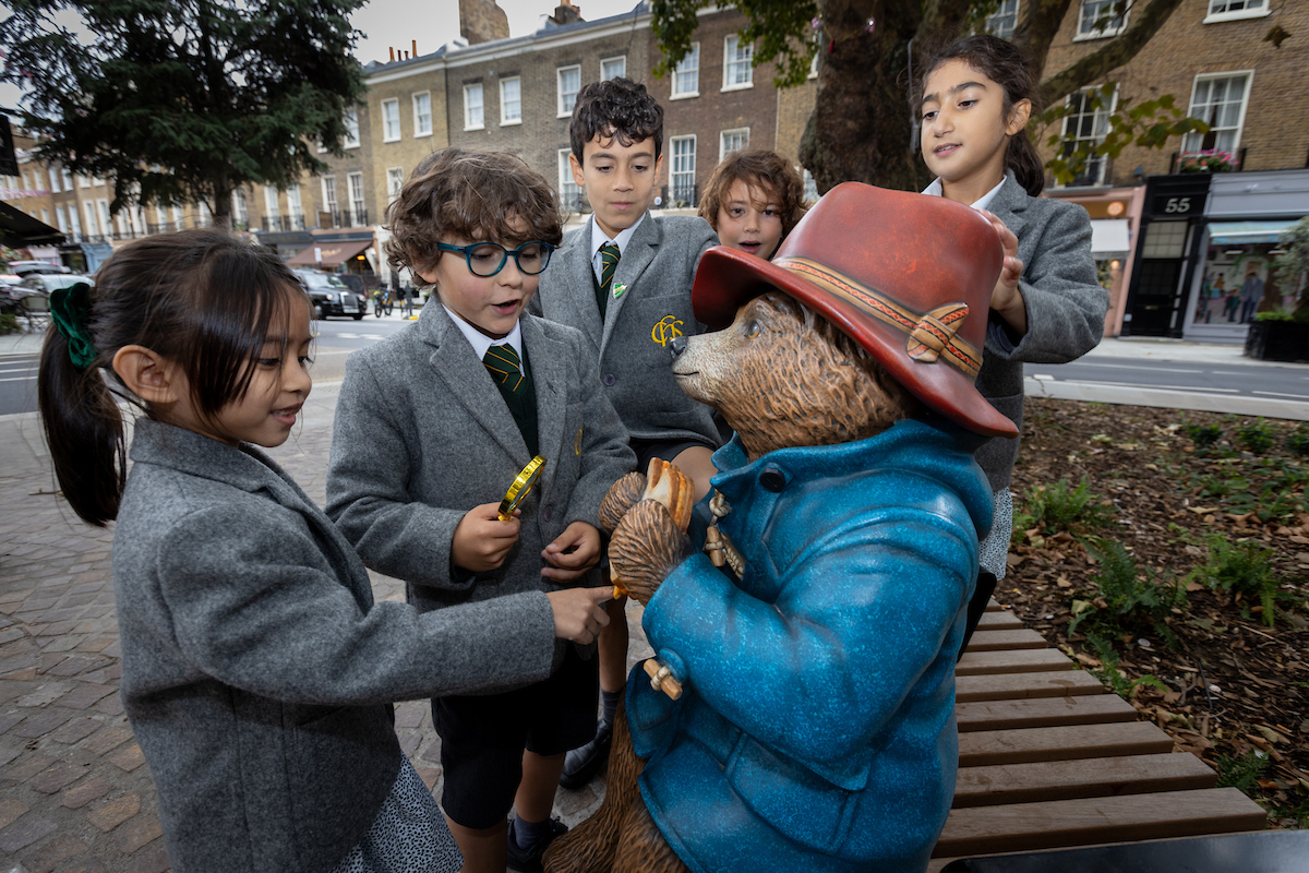 school children interacting with a paddington bear statue