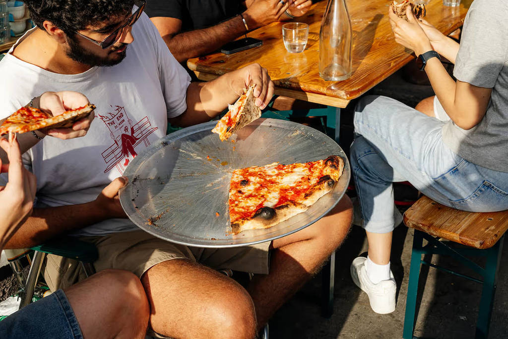 Menschen sitzen im Sonnenschein und genießen eine köstlich aussehende Pizza